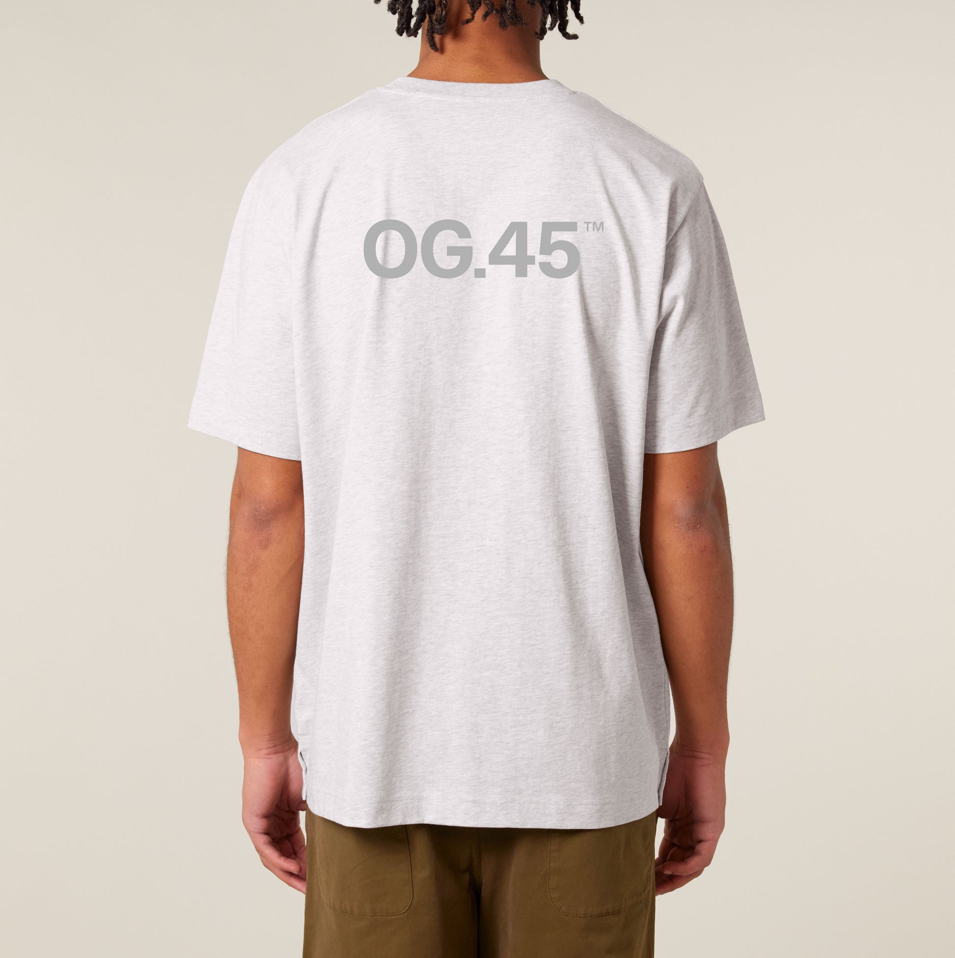 Bagsiden af lysegrå T-shirt med stort OG.45™ tryk mellem skuldrene, båret af mand stående mod neutral baggrund.